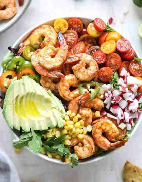 A colorful shrimp taco bowl filled with spicy grilled shrimp, cherry tomatoes, corn, avocado, jalape...