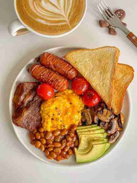 🥓🍳 A hearty breakfast plate with scrambled eggs 🥚, crispy bacon 🥓, grilled sausages 🌭, baked be...