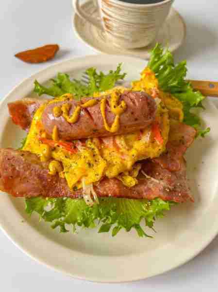 Savory breakfast sandwich with fluffy scrambled eggs, grilled sausage, and crispy bacon on a bed of...
