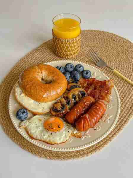 A hearty breakfast plate 🥯🍳 — toasted bagel with cream cheese, crispy bacon, juicy sausages, sauté...